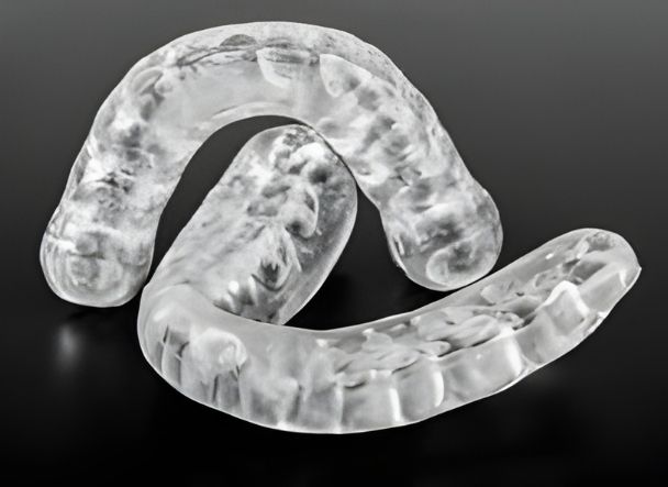 Dos férulas de descarga transparentes para bruxismo apoyadas sobre fondo negro, mostrando el contorno de las arcadas dentales.