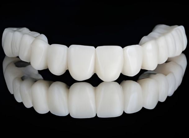 Prótesis dental completa con dos arcadas de dientes blancos alineados sobre fondo negro.